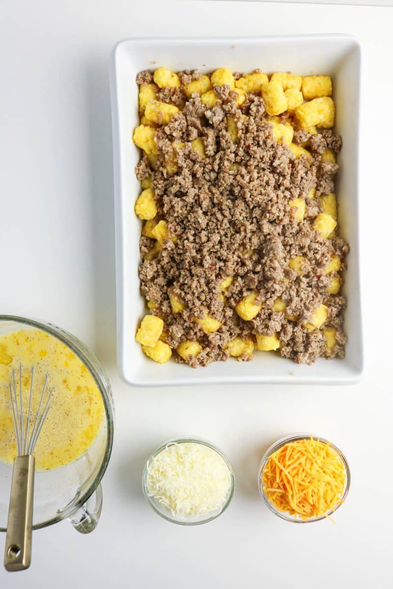 Cooked breakfast sausage mixed with frozen tater tots in a baking dish. Hostess At Heart