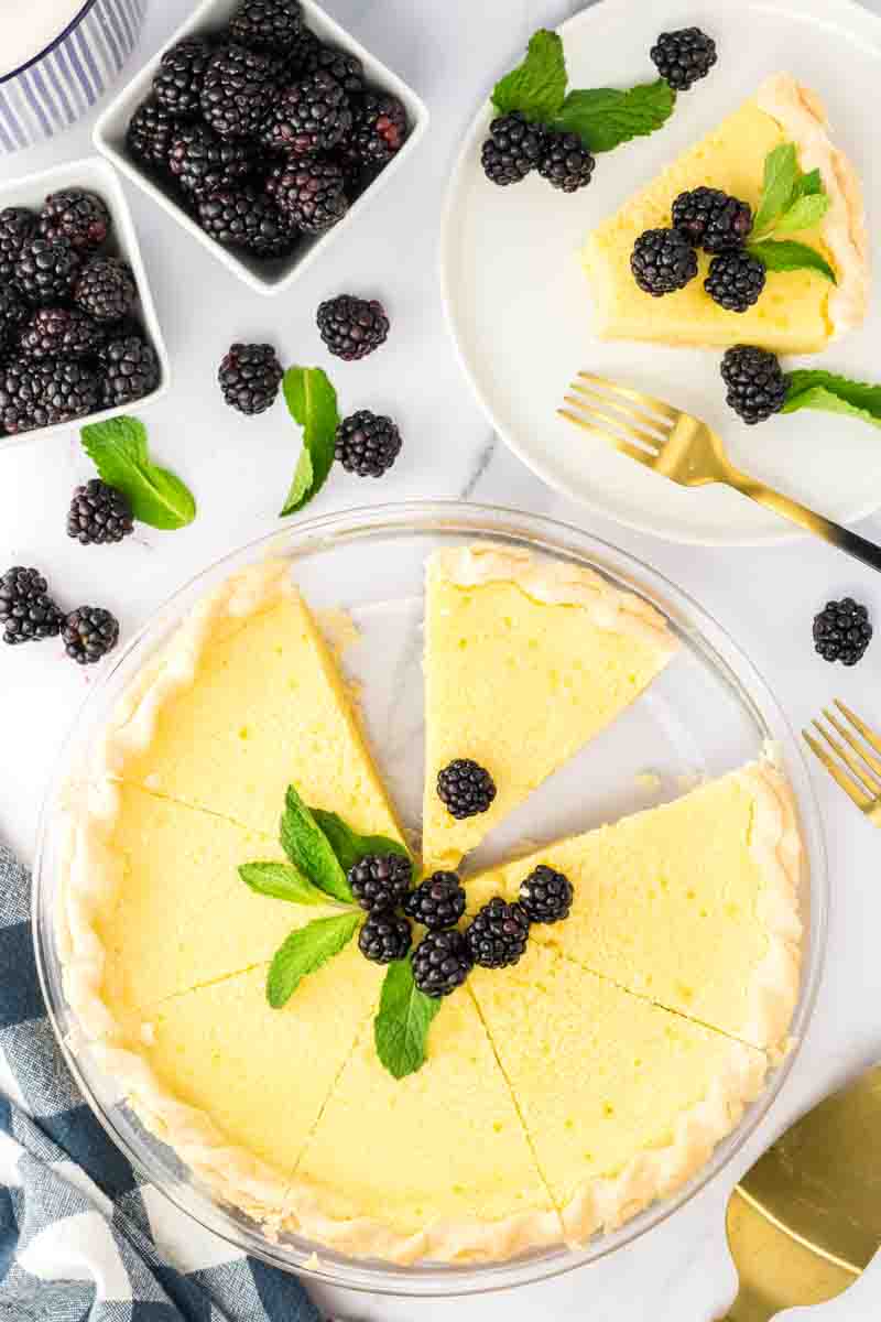 Top down view of a southern buttermilk pie with a slice missing. It's garnished with fresh blackberries and mint. Hostess At Heart