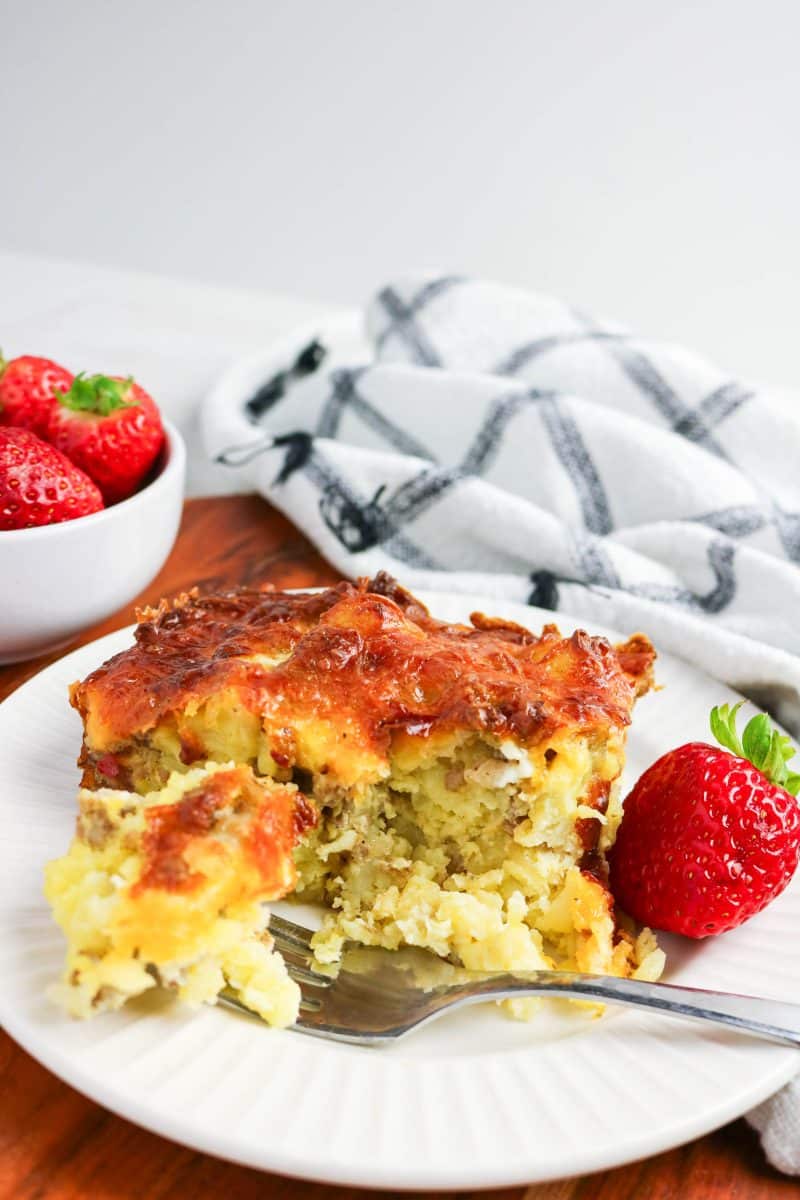 A fork taking out a bite of baked breakfast tater tot casserole under a crispy cheese topping. Hostess At Heart