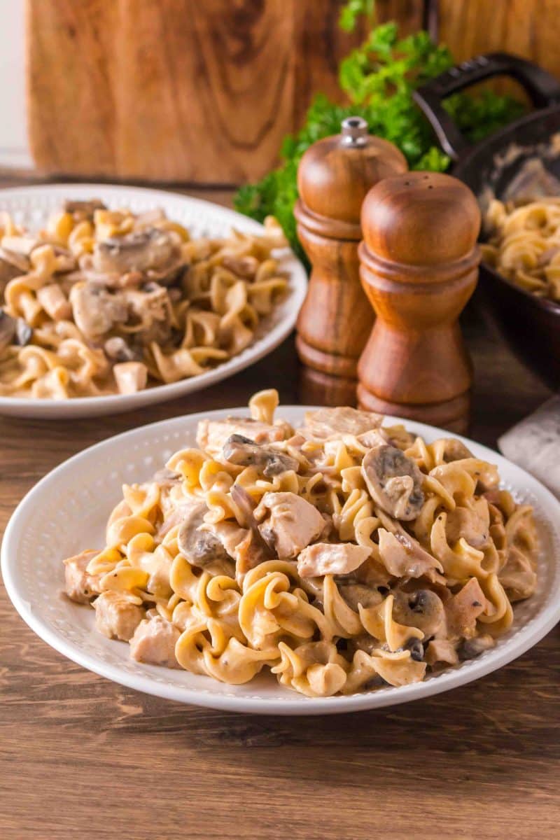 Angled view of a white serving dish filled with Turkey stroganoff with leftover turkey, mushrooms, and egg noodles. Hostess At Heart