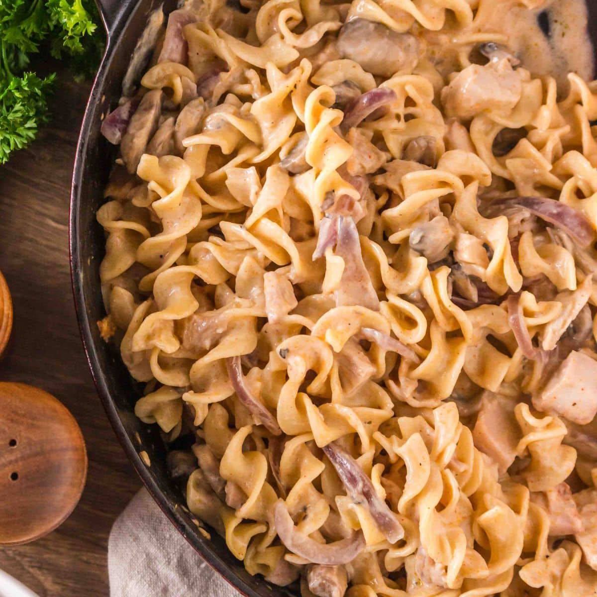 Top down view of a cast-iron skillet filled with creamy turkey stroganoff with mushrooms and egg noodles. Hostess At Heart