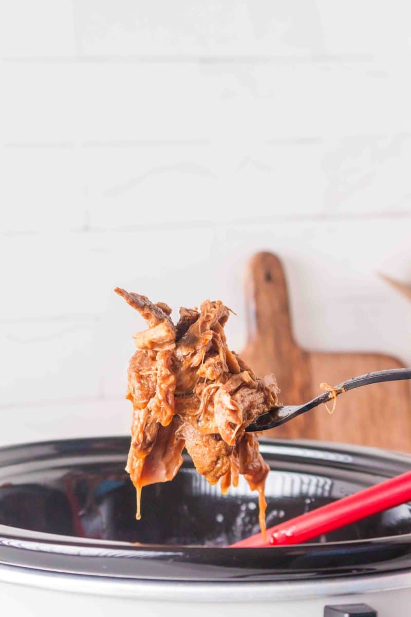 Juicy finished BBQ pulled pork being lifted out of the slow cooker with a fork. Hostess At Heart