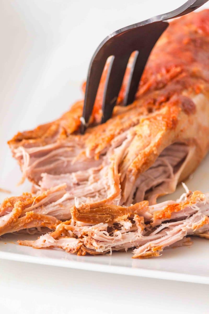 Cooked pork tenderloin being shredded with a fork. Hostess At Heart