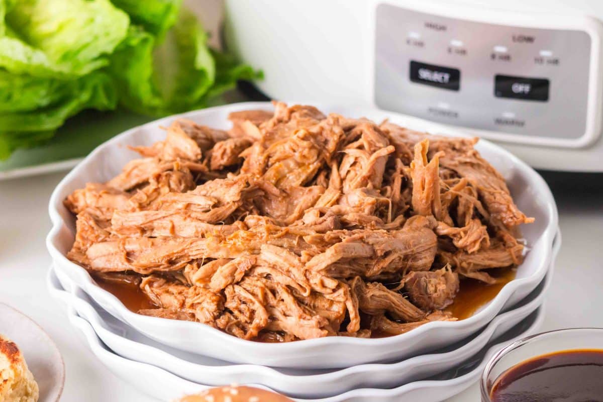 Tender shredded BBQ pork tenderloin on a white serving dish. Hostess At Heart